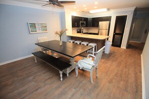 A dining area with a table, benches, and chairs, a kitchen with appliances, and a ceiling fan. - High 5! Mainsail Townhome! Dedicated covered parking Private Beach! FREE beach set up included. (Destin)