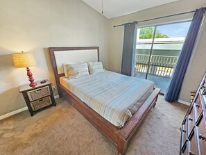 A bedroom with a bed, a nightstand, a lamp, a dresser, and a balcony with a view. - High 5! Mainsail Townhome! Dedicated covered parking Private Beach! FREE beach set up included. (Destin)