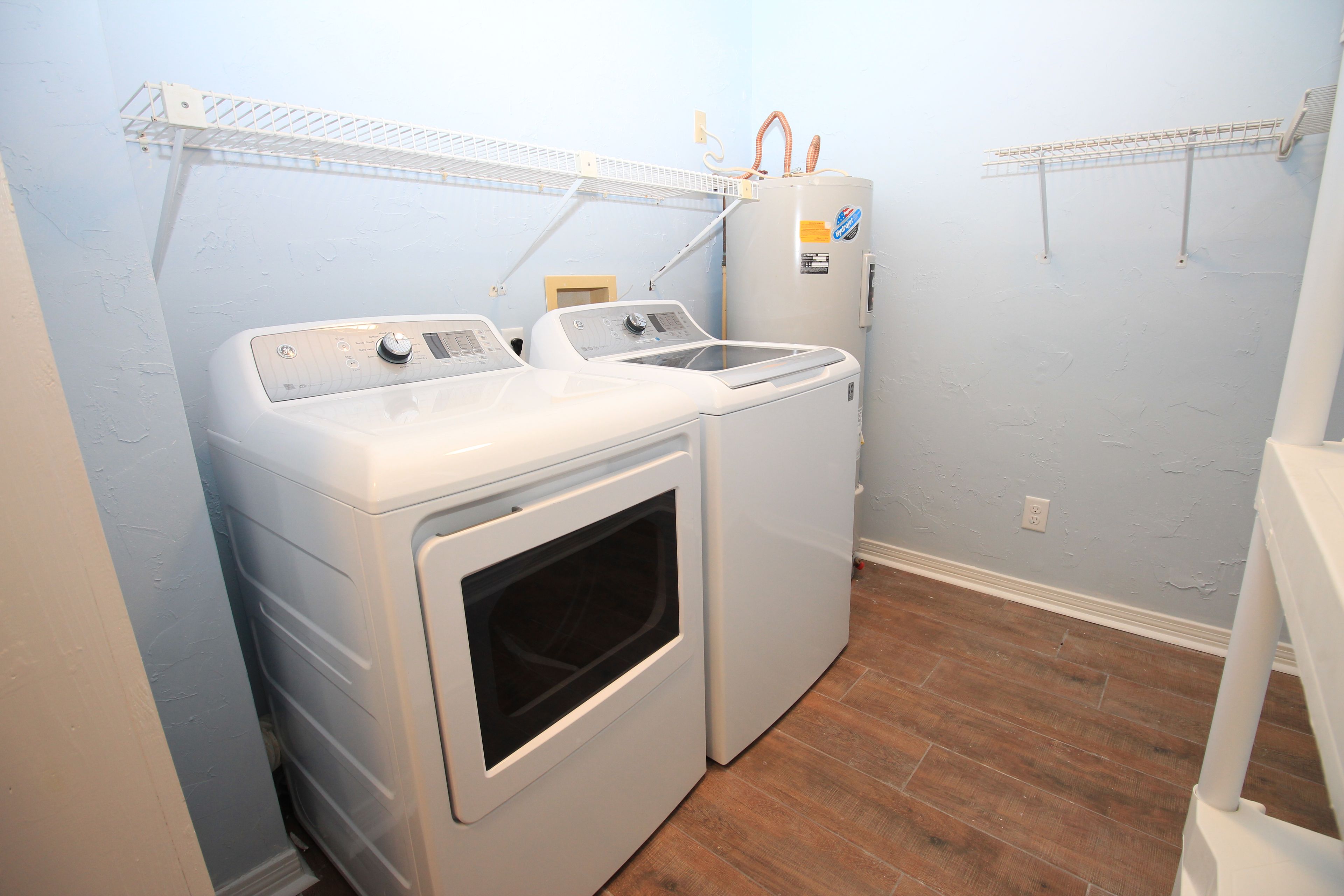 Une buanderie équipée de deux machines à laver à chargement frontal et d’un sèche-linge, avec un plancher en bois et des murs de couleur bleu clair.
