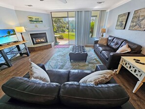 A living room with a fireplace, leather sofas, a television, and a view of the outdoors.