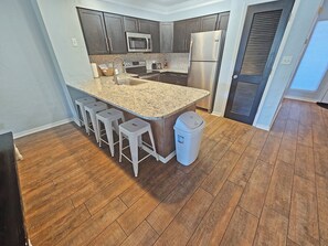 A kitchen with dark wood cabinets, stainless steel appliances, a granite countertop, and a trash can.