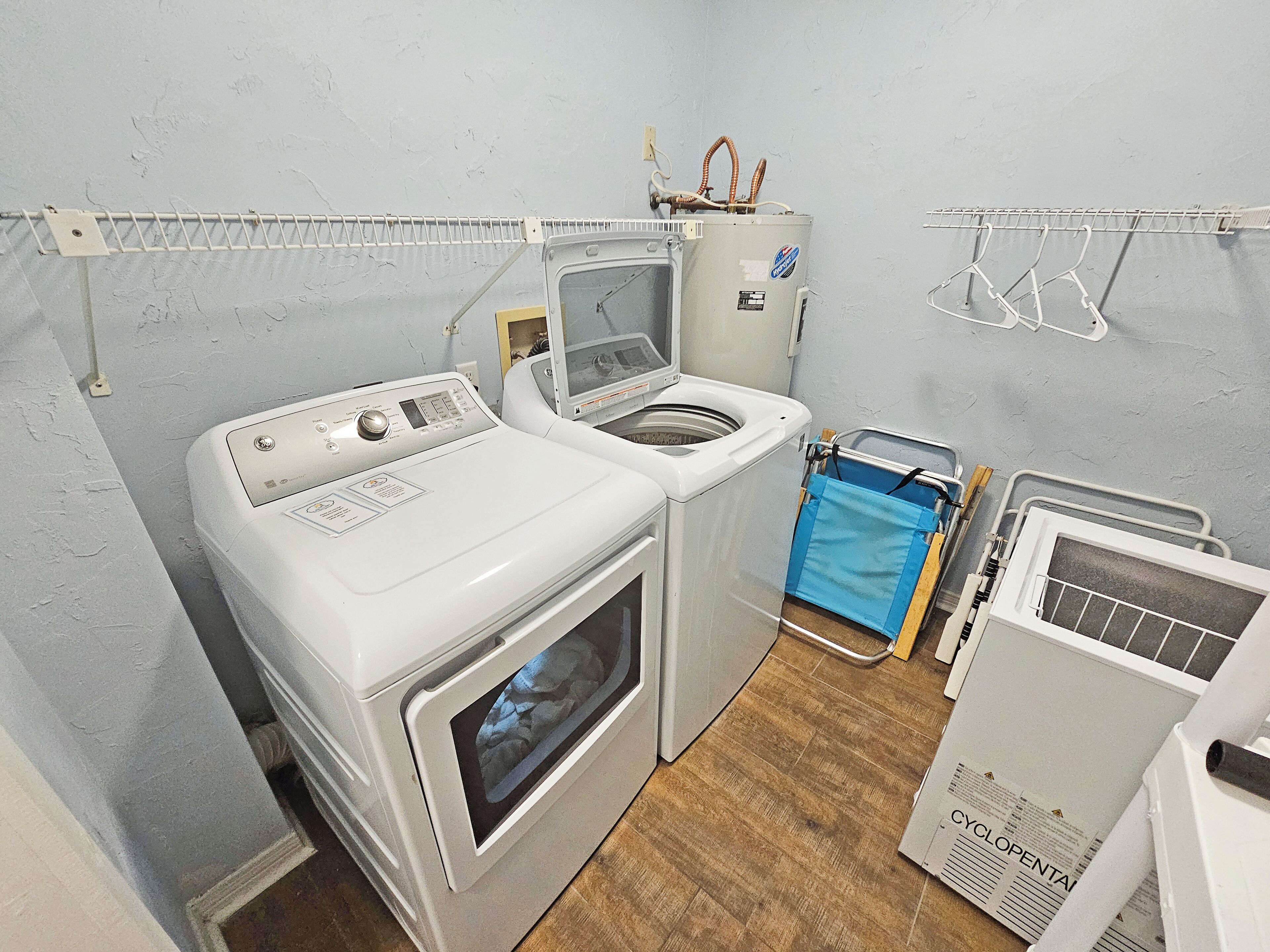 A laundry room with a front-loading washer and dryer, a drying rack, and a recycling bin.