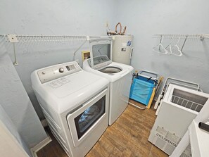A laundry room with a front-loading washer and dryer, a drying rack, and a recycling bin. - High 5! Mainsail Townhome! Dedicated covered parking Private Beach! FREE beach set up included. (Destin)