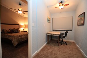 A bedroom with a bed, a desk, and a ceiling fan.