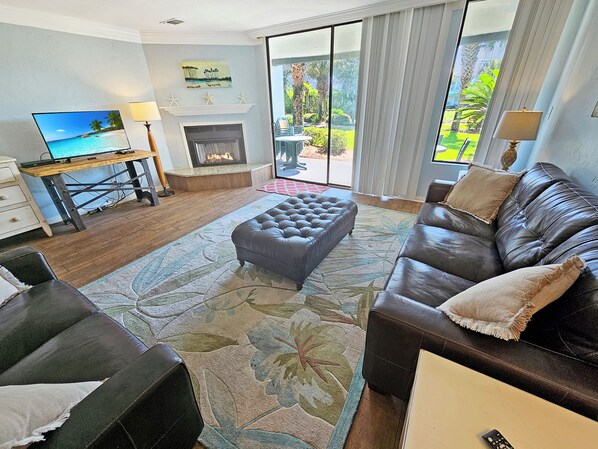 A living room with a fireplace, a television, and a view of the outdoors. - High 5! Mainsail Townhome! Dedicated covered parking Private Beach! FREE beach set up included. (Destin)