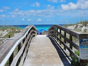 A wooden boardwalk leading to beach umbrellas and a signboard. - High 5! Mainsail Townhome! Dedicated covered parking Private Beach! FREE beach set up included. (Destin)