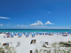 A beach with numerous blue umbrellas and white lounge chairs, a clear blue sky, and a calm sea. - High 5! Mainsail Townhome! Dedicated covered parking Private Beach! FREE beach set up included. (Destin)