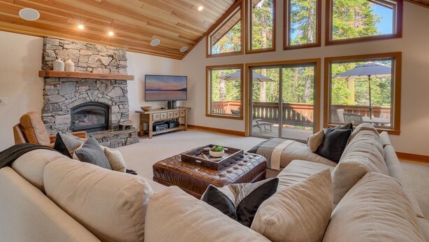 A cozy living room with a stone fireplace, comfortable seating, and large windows offering a view of the outdoors. - Tahoe Treehouse - TLUXP (Homewood)