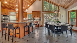 A modern kitchen with wooden cabinets, stainless steel appliances, and a bar area with stools. - Tahoe Treehouse - TLUXP (Homewood)
