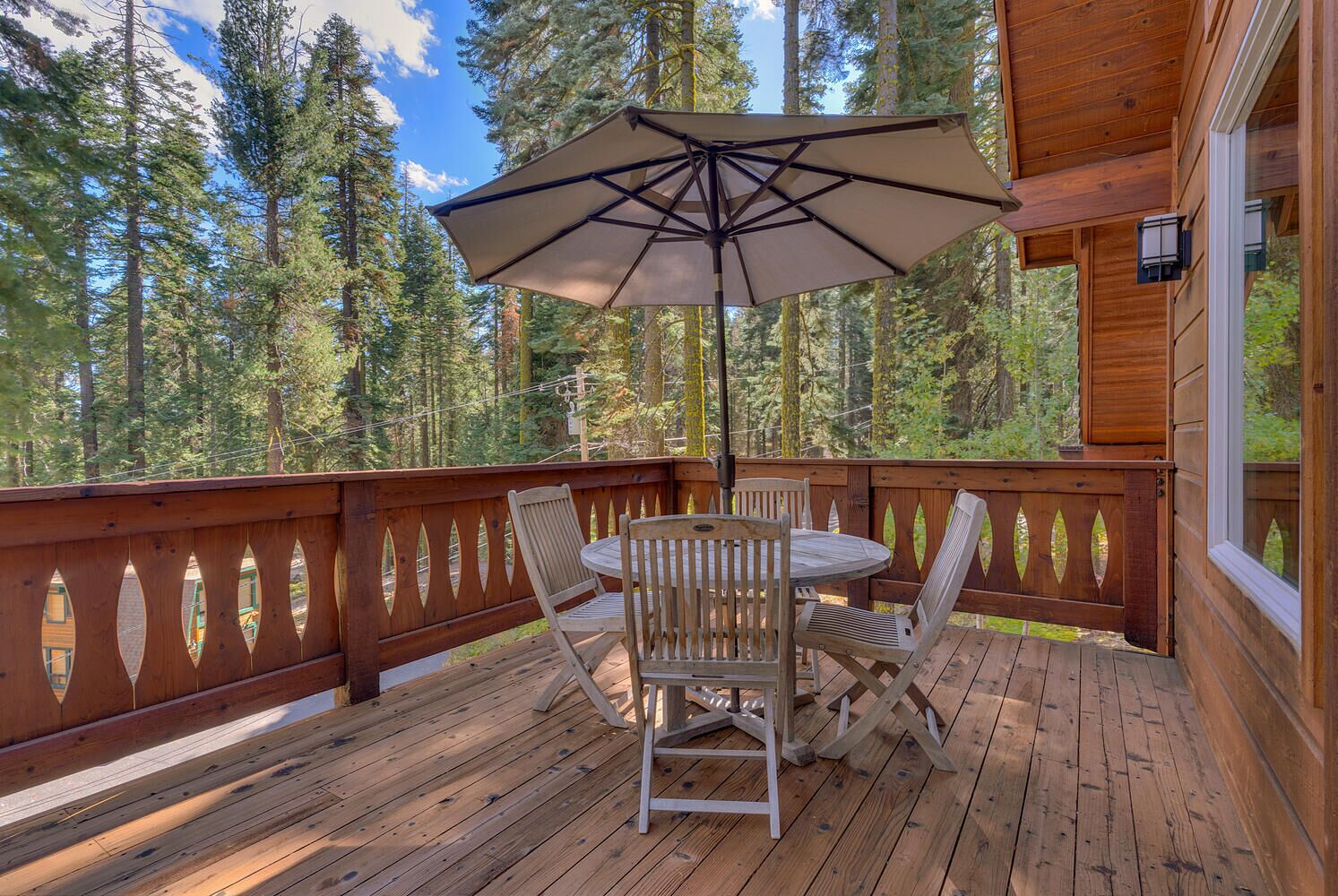 Une terrasse en bois avec une table et des chaises, un parasol et une vue sur une forêt.