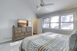 A bedroom with a bed, dresser, TV, ceiling fan, and a window with blinds.