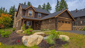 A two-story log cabin with a garage, surrounded by a landscaped garden with rocks and plants. - Relax in LUXURY! *Fantastic Discounts* Centrally located in the Resort! (Cle Elum)