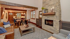 A spacious living area with a stone fireplace, wooden furniture, and a kitchen in the background. - Relax in LUXURY! *Fantastic Discounts* Centrally located in the Resort! (Cle Elum)