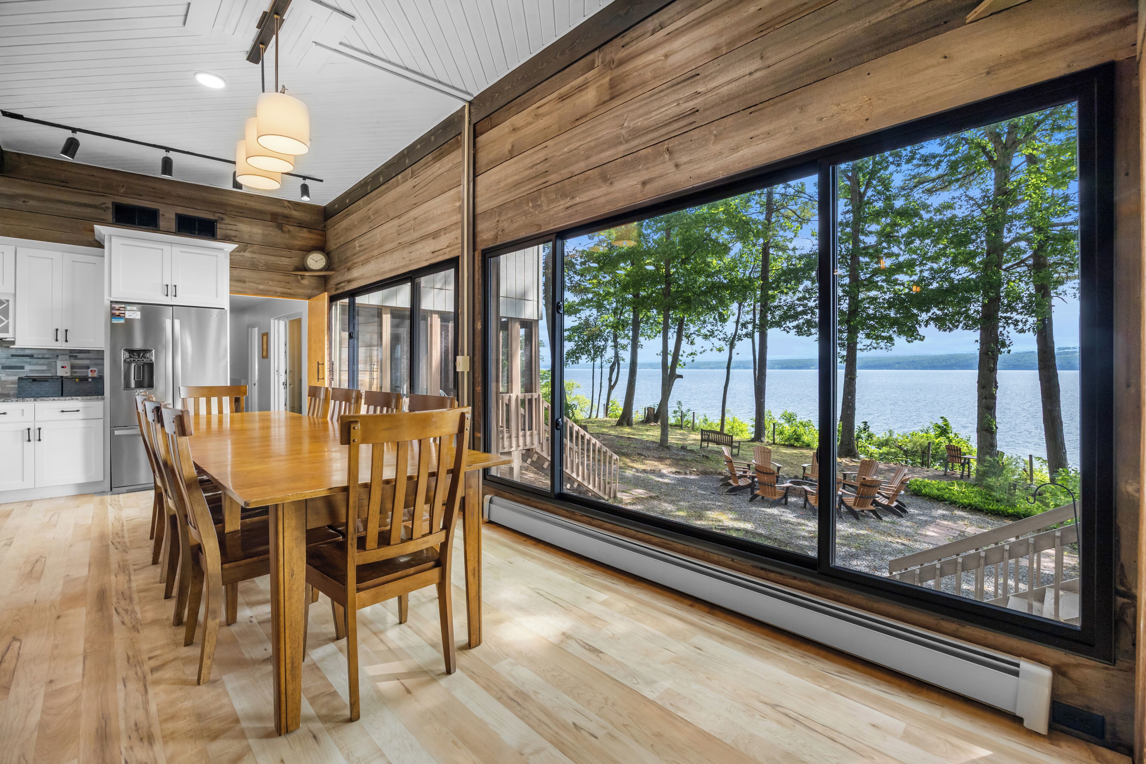 A modern kitchen with a large dining table and chairs, a stainless steel refrigerator, and a view of a lakeside deck.
