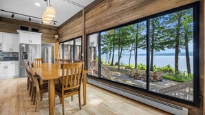 Une cuisine moderne dotée d’une grande table à manger et de chaises, d’un réfrigérateur en acier inoxydable et offrant une vue sur une terrasse au bord du lac.