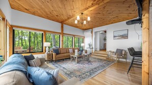 Un vaste espace de vie doté d’un plafond en bois, de grandes fenêtres, d’un canapé, d’une table basse et d’un tapis.