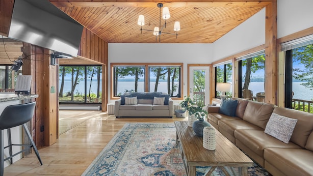 Un vaste espace de vie doté d’un plafond en bois, de grandes fenêtres, d’un canapé, d’une table basse et d’une vue sur un lac.