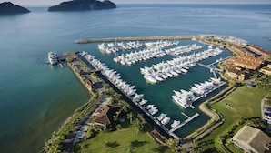 Une vue aérienne d’une marina où sont amarrés de nombreux bateaux, le tout étant entouré d’un paysage côtier composé de bâtiments et de verdure.