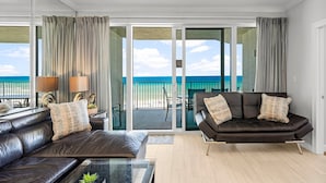 Een moderne woonkamer met een leren bank en fauteuil, een glazen salontafel, en uitzicht op de oceaan door grote schuifdeuren.