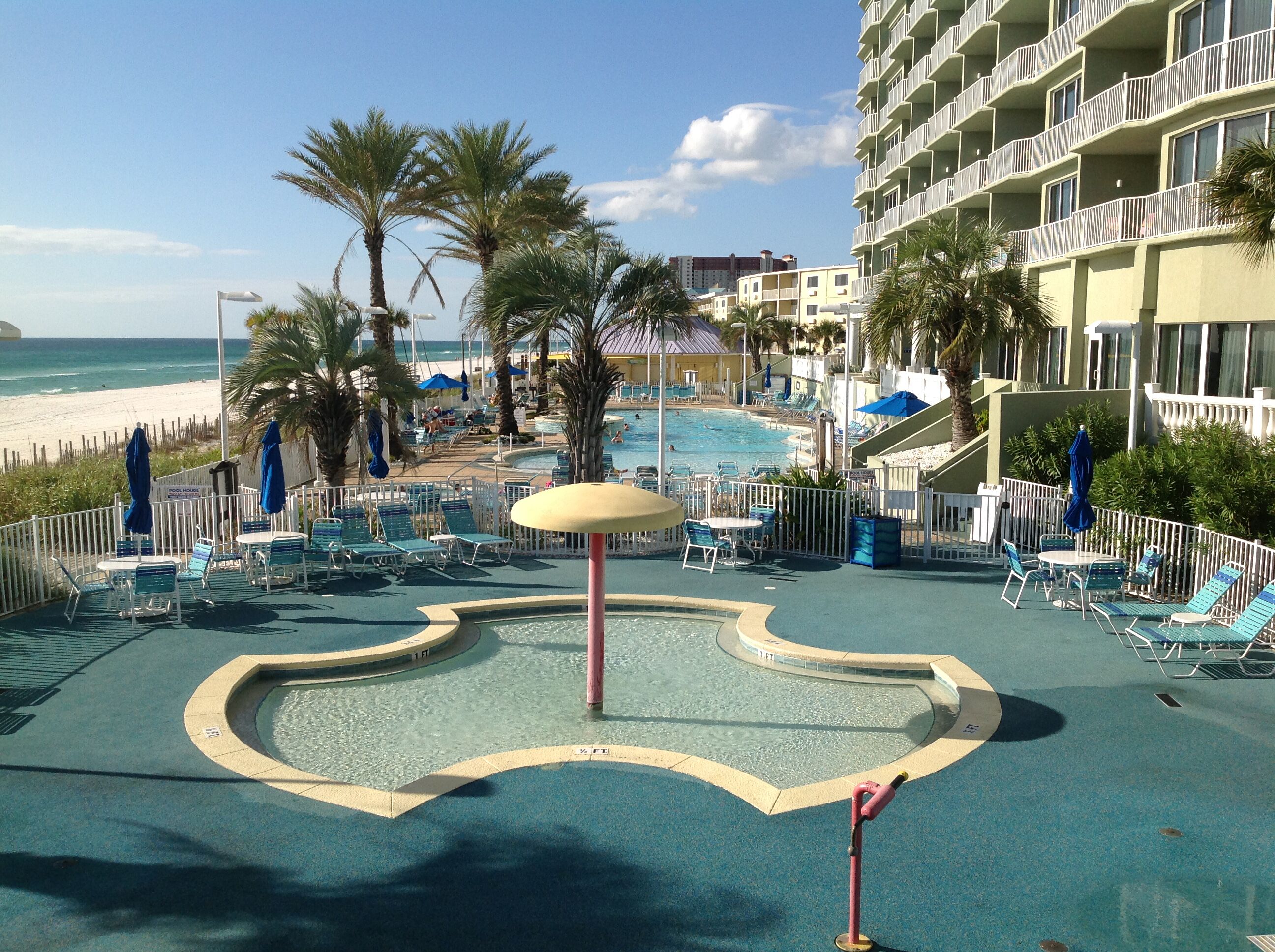 Un espace piscine avec des chaises longues et des parasols, une petite piscine et une vue sur la plage et l’océan.