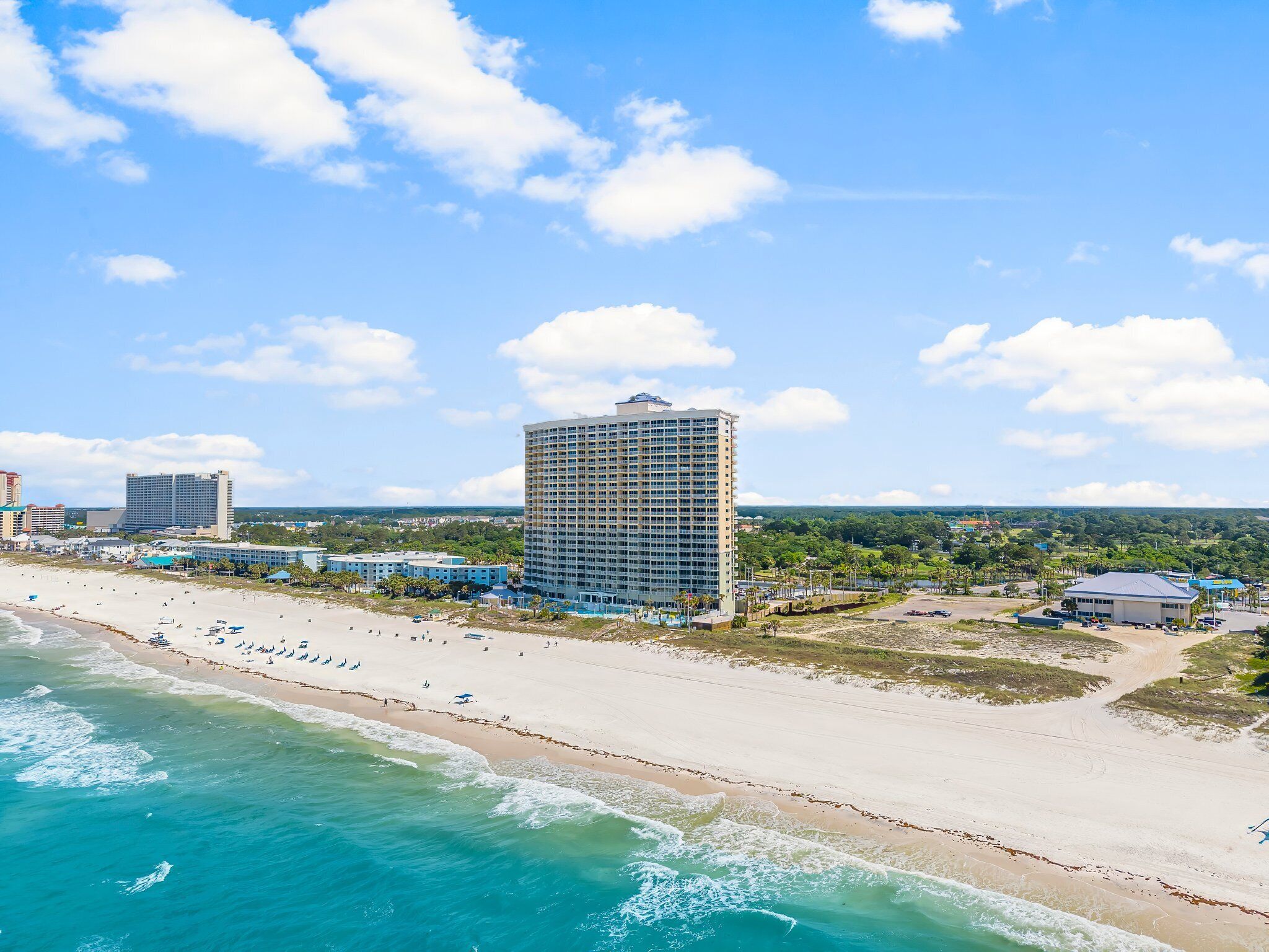 A beachfront hotel with a large building, a sandy beach, and ocean waves.