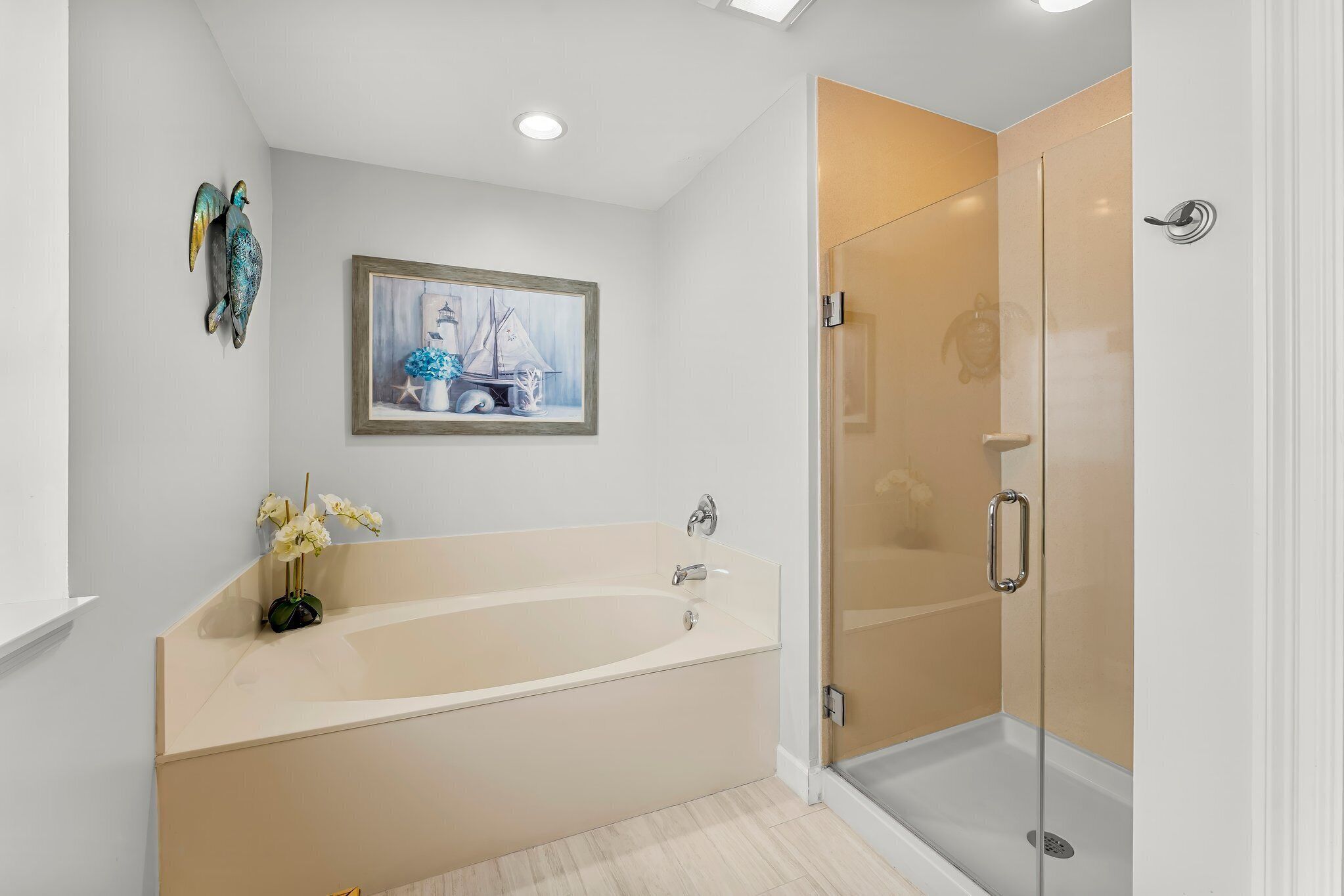 A modern bathroom with a freestanding bathtub, a glass-enclosed shower, and a framed painting above the bathtub.