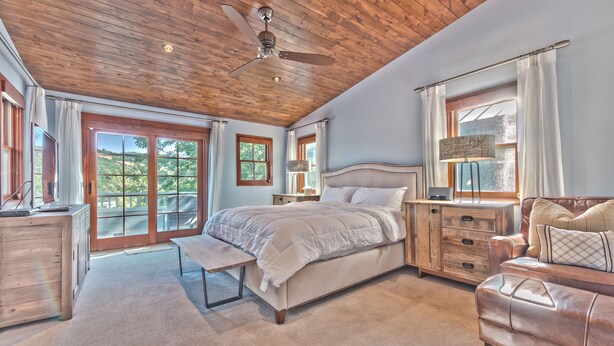 Une chambre à coucher comprenant un lit, des tables de chevet, un banc, une commode et une vue sur l’extérieur.
