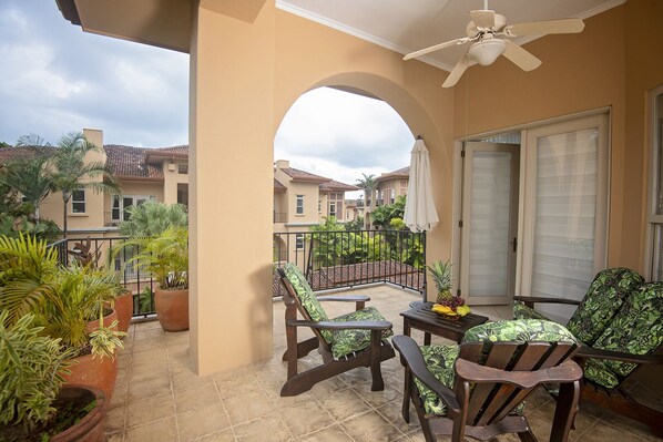A balcony with chairs, potted plants, and a table with fruit.