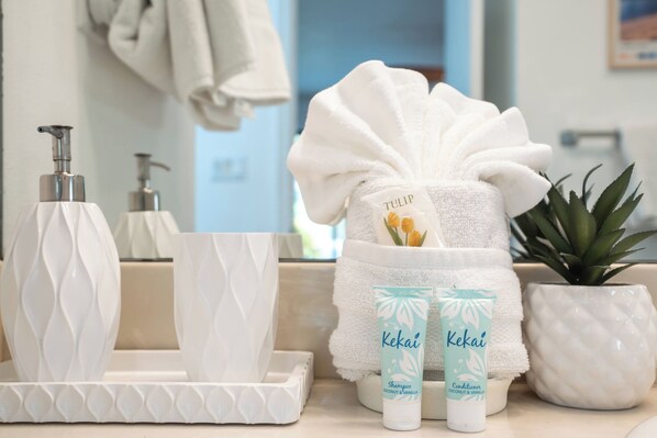 Ein Badezimmer-Waschtisch mit einem weißen Handtuch, zwei Flaschen Kekaï Shampoo und Conditioner, einer Topfpflanze und einer weißen Seifenspender.