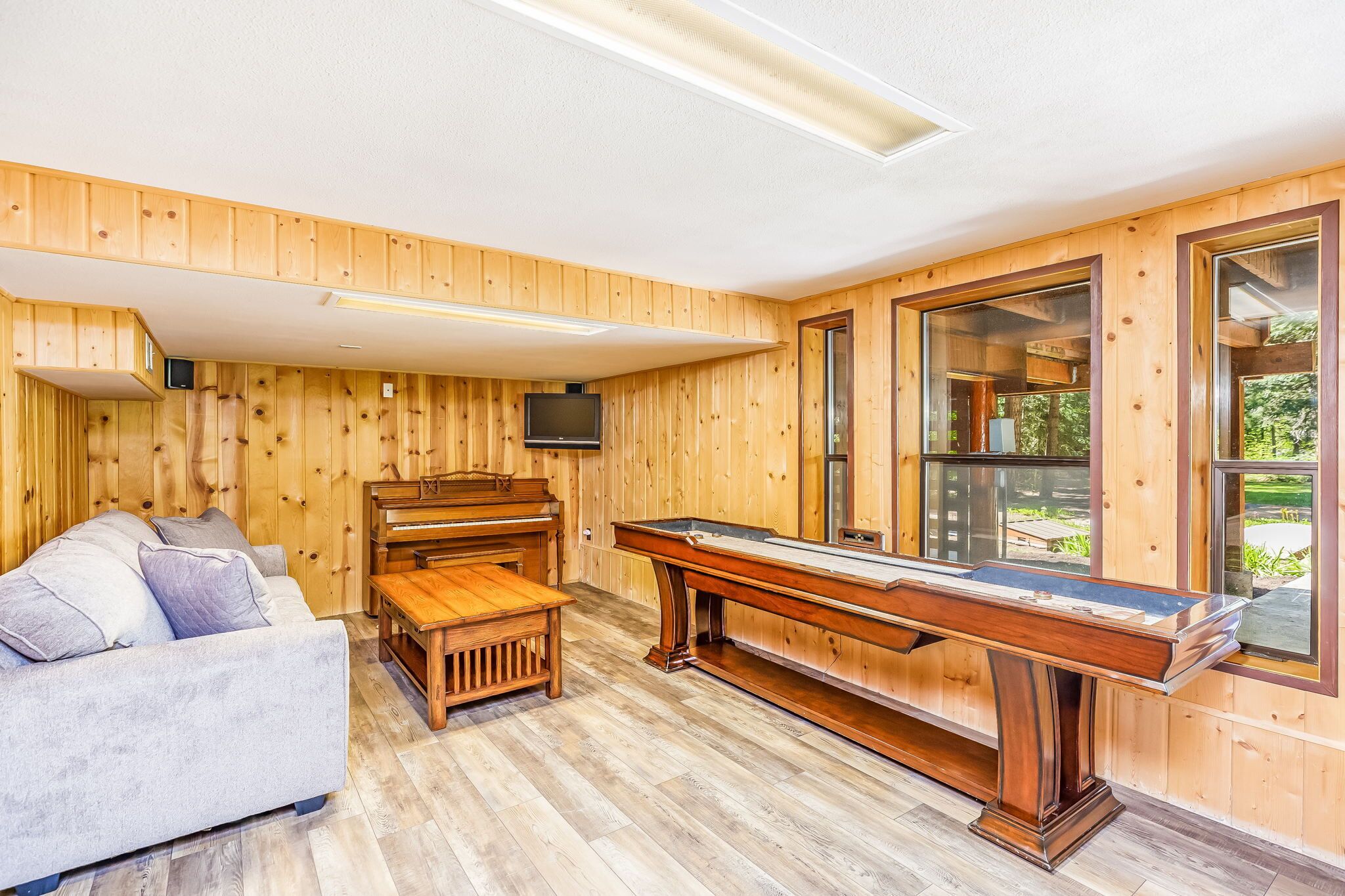 A wooden-paneled room with a pool table, a sofa, and a television.
