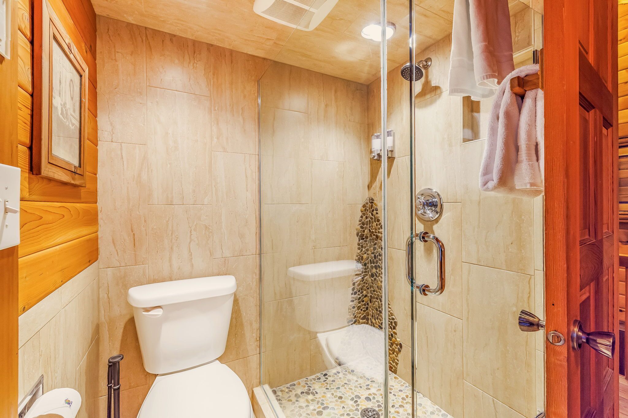 A bathroom with a toilet, a shower with a glass door, and a wooden wall.