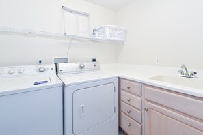 A laundry area with a washing machine, a dryer, a sink, and a wooden cabinet. - Open concept, private beach access w/resort amenities! 🏖️ (Destin)