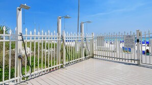 Area spiaggia recintata con staccionata bianca, cartello che indica l'obbligo di braccialetto e chiave di sicurezza, e cielo azzurro.