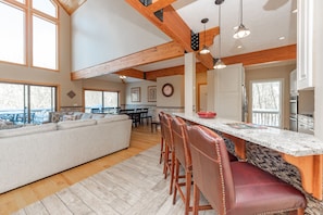 A spacious kitchen with a large island, wooden beams, and a dining area with a sofa and chairs.