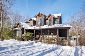 A large, multi-story wooden house with a covered porch and a snow-covered roof.