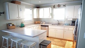 A modern kitchen with white cabinets, a central island with stools, a dishwasher, and a coffee maker. - Gulf Winds Down 3/2 in Grayton, comm.pool, short walk to beach (Santa Rosa Beach)