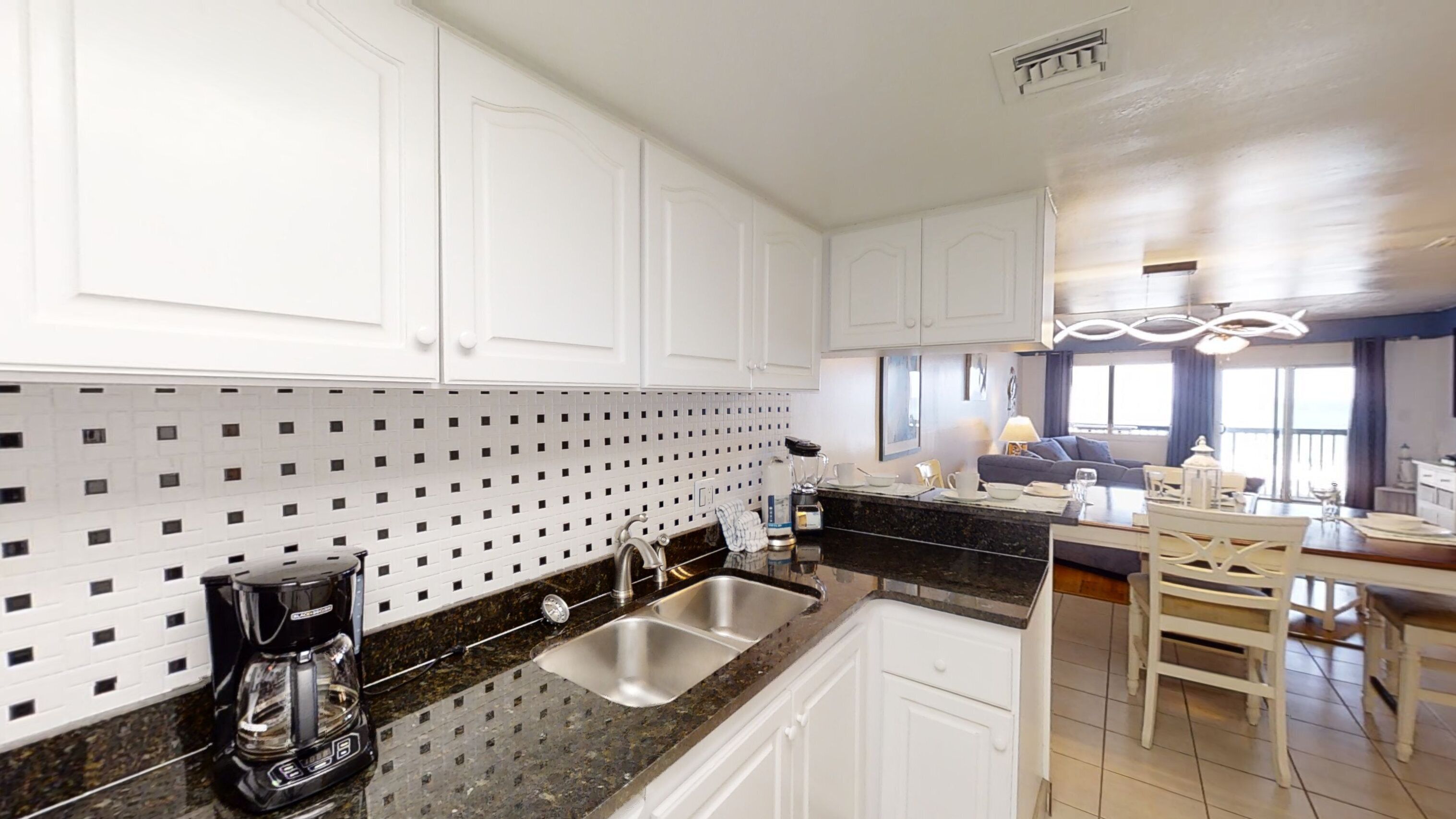 A modern kitchen with white cabinets, a black granite countertop, and a double sink.