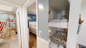Una habitación con literas, baño con cortina de ducha y un cartel con motivos playeros en la pared.