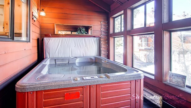 Eine Holzhütte mit Whirlpool, großen Fenstern und Blick ins Freie.