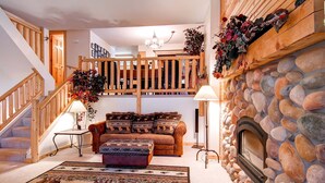 Ein gemütliches Wohnzimmer mit Kamin, Treppe und einer Couch mit gemusterten Kissen.