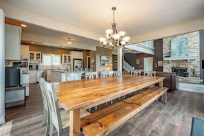 A spacious kitchen with a large wooden table, white cabinets, and a stone fireplace.