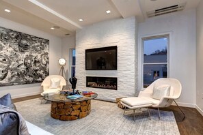 A modern living room with a stone coffee table, a fireplace, a large abstract painting, and a white chair.