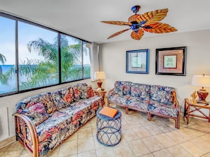 A room with a large window, a ceiling fan, two sofas with floral upholstery, and a small round table.