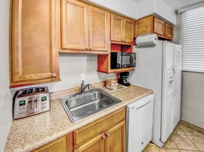 A compact kitchen with wooden cabinets, a stainless steel sink, a coffee maker, and a white dishwasher.