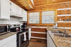 Una cocina con armarios blancos, encimera de granito, electrodomésticos de acero inoxidable y vigas de madera.