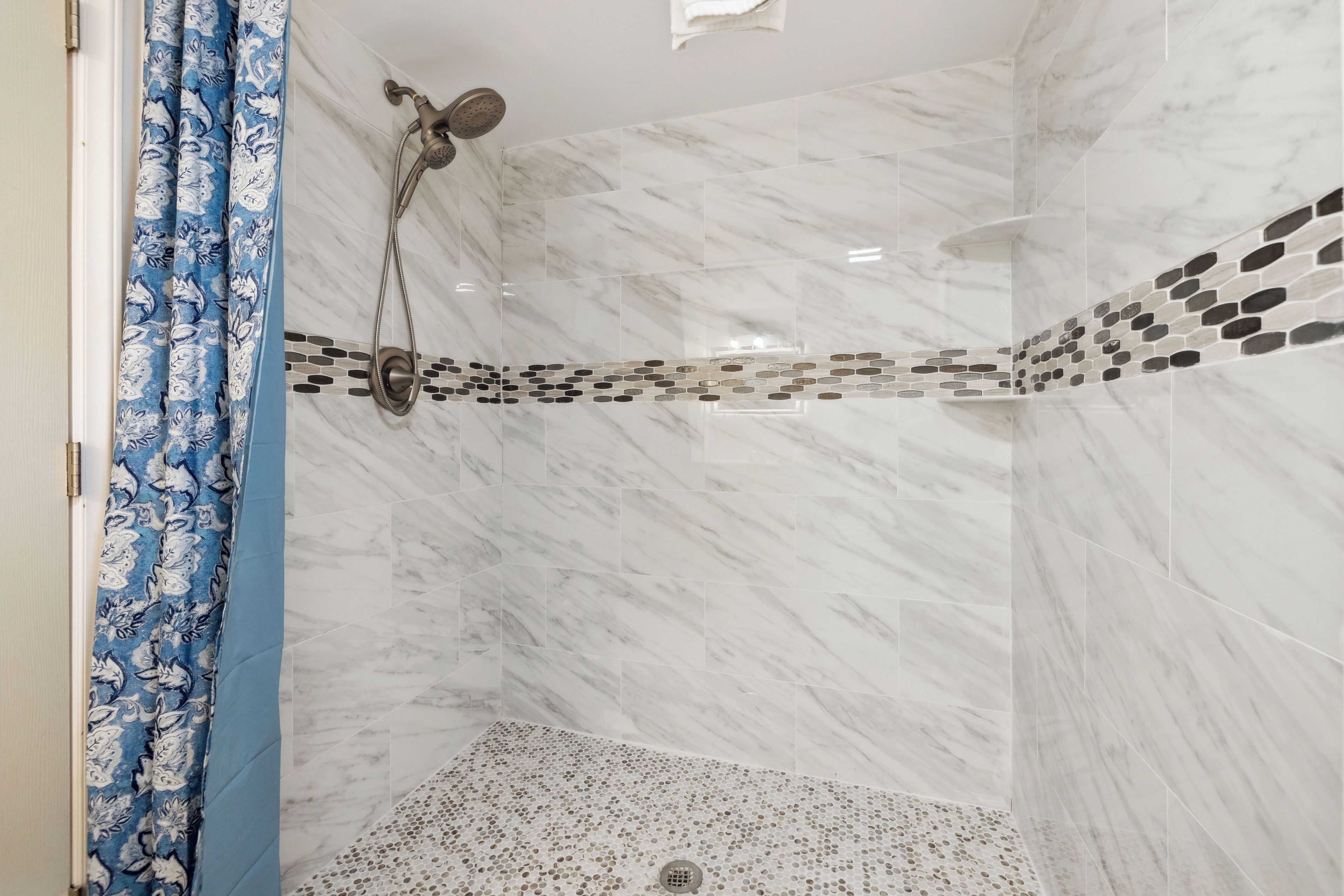 Eine Dusche mit Regendusche, Ablaufrinne und Fliesenboden mit dekorativem Mosaikstreifen.