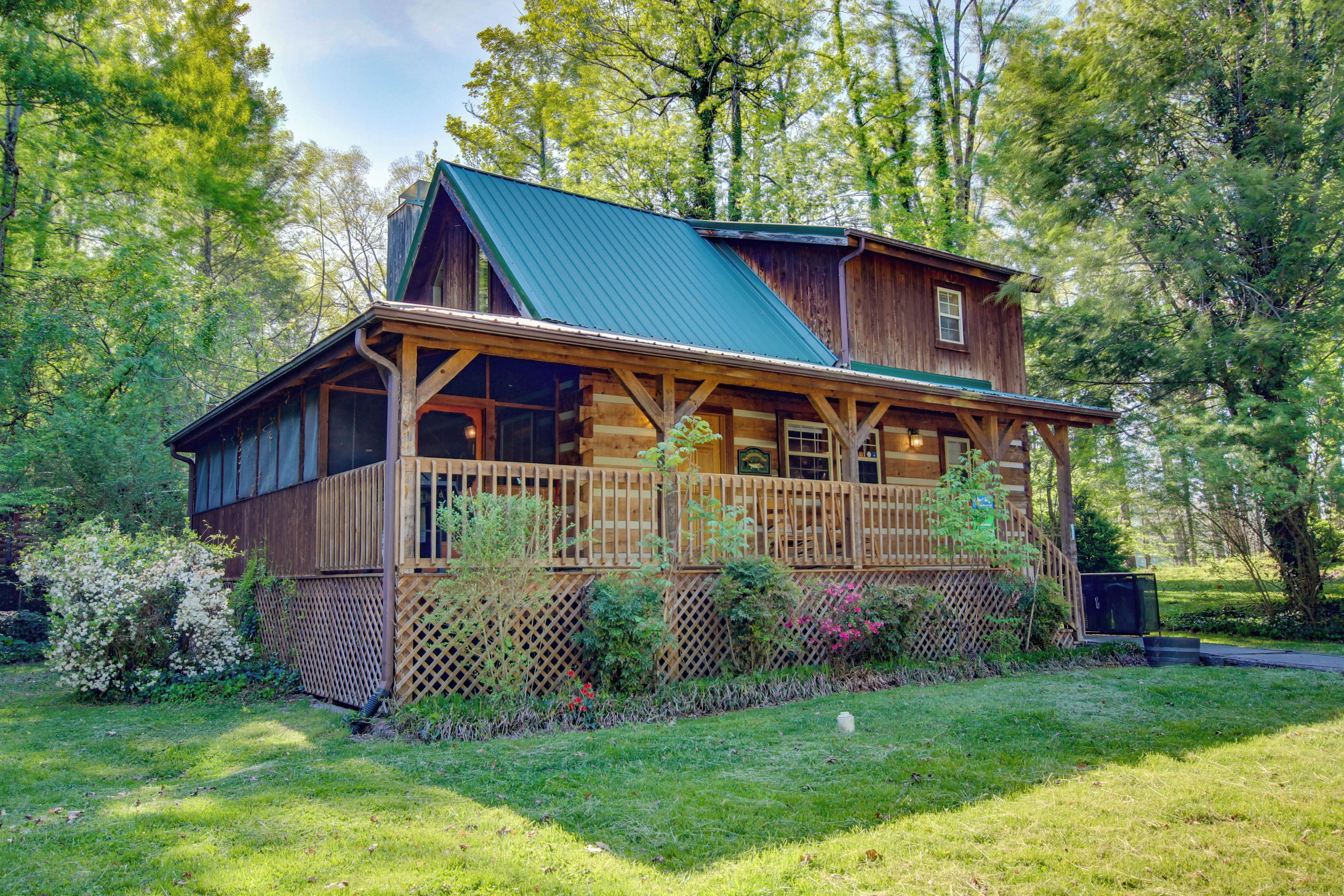 A log cabin with a green roof, wooden deck, and a fenced yard.