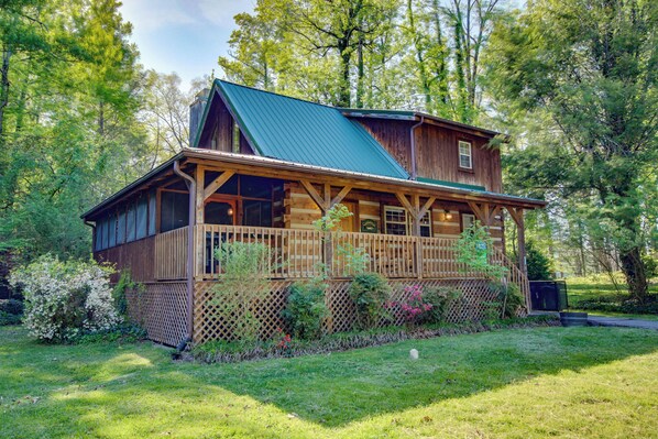 A log cabin with a green roof, wooden deck, and a fenced yard.