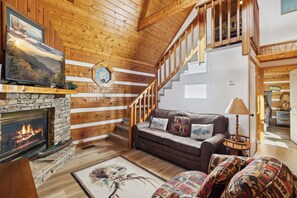 Una sala acogedora con chimenea, paredes de madera, una escalera y un sofá cómodo.