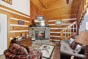 Un salón acogedor con chimenea de piedra, paredes de madera, un sofá cómodo y una escalera.